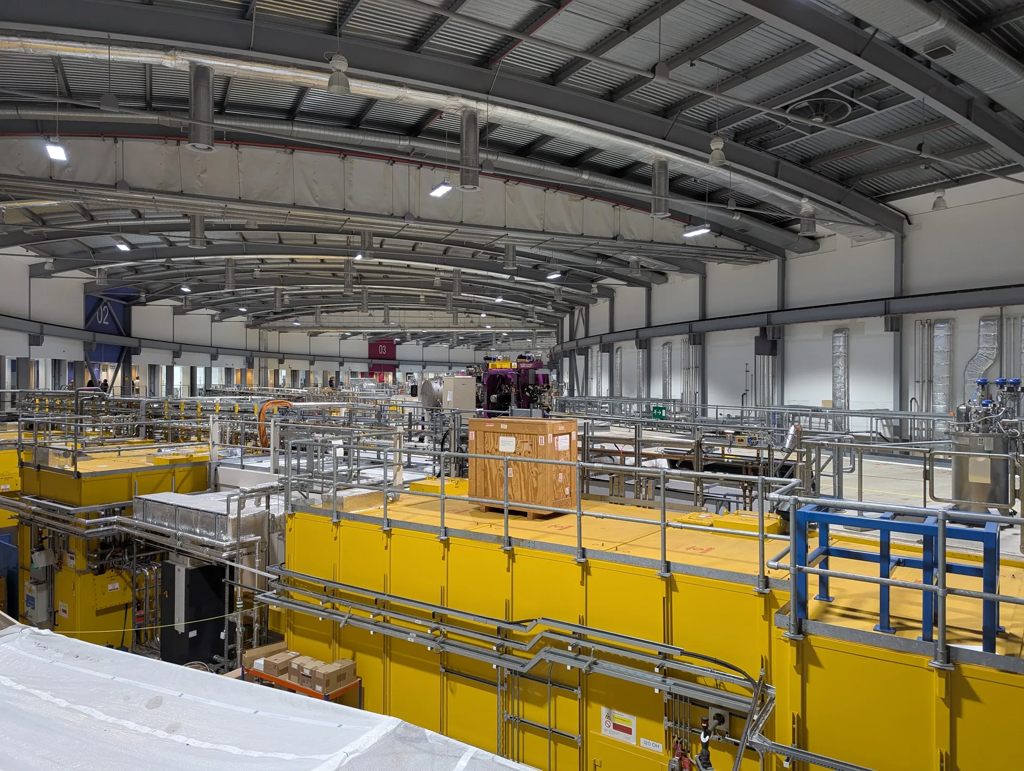 The experimental hall at Diamond Light Source, with yellow-clad beamline hutches curving around the synchrotron storage ring
