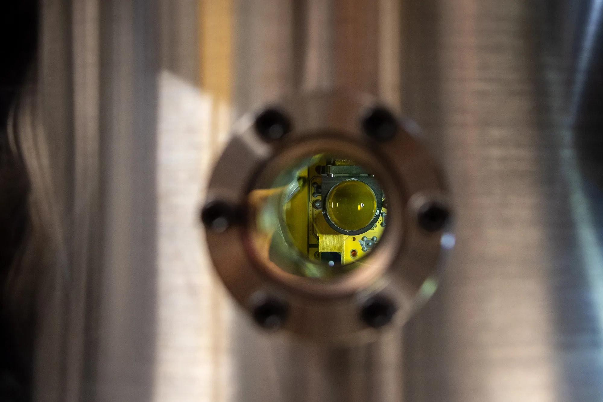 View through a vacuum chamber viewport at the National Quantum Computing Centre, showing the gold-toned ion trap assembly inside