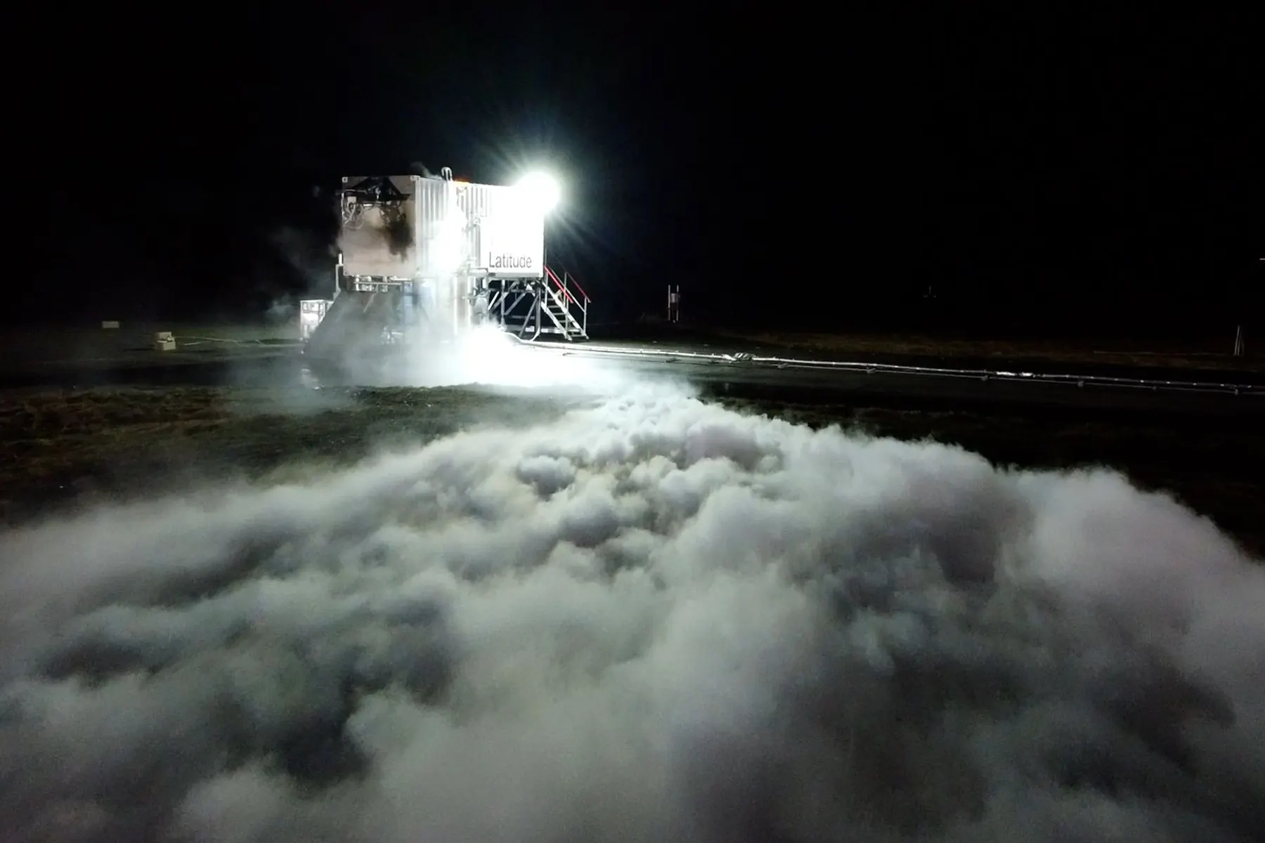 A rocket engine firing horizontally at night on a test stand, exhaust plume lit against the dark