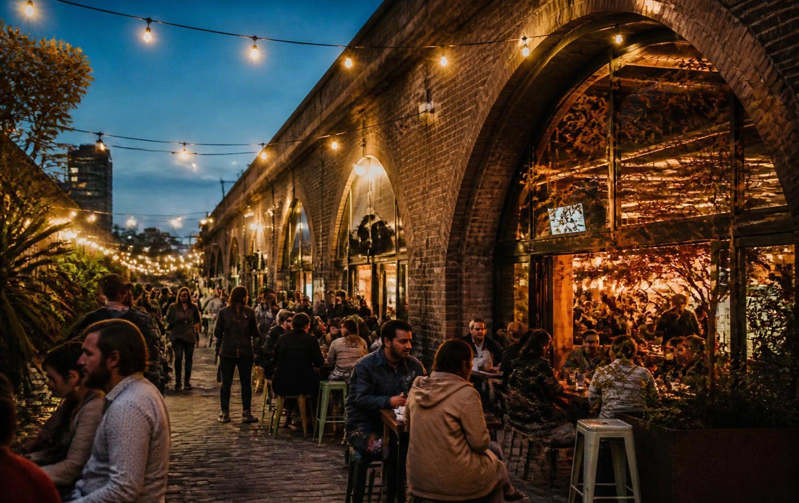 A northern city evening: people eating under string lights beneath brick railway arches